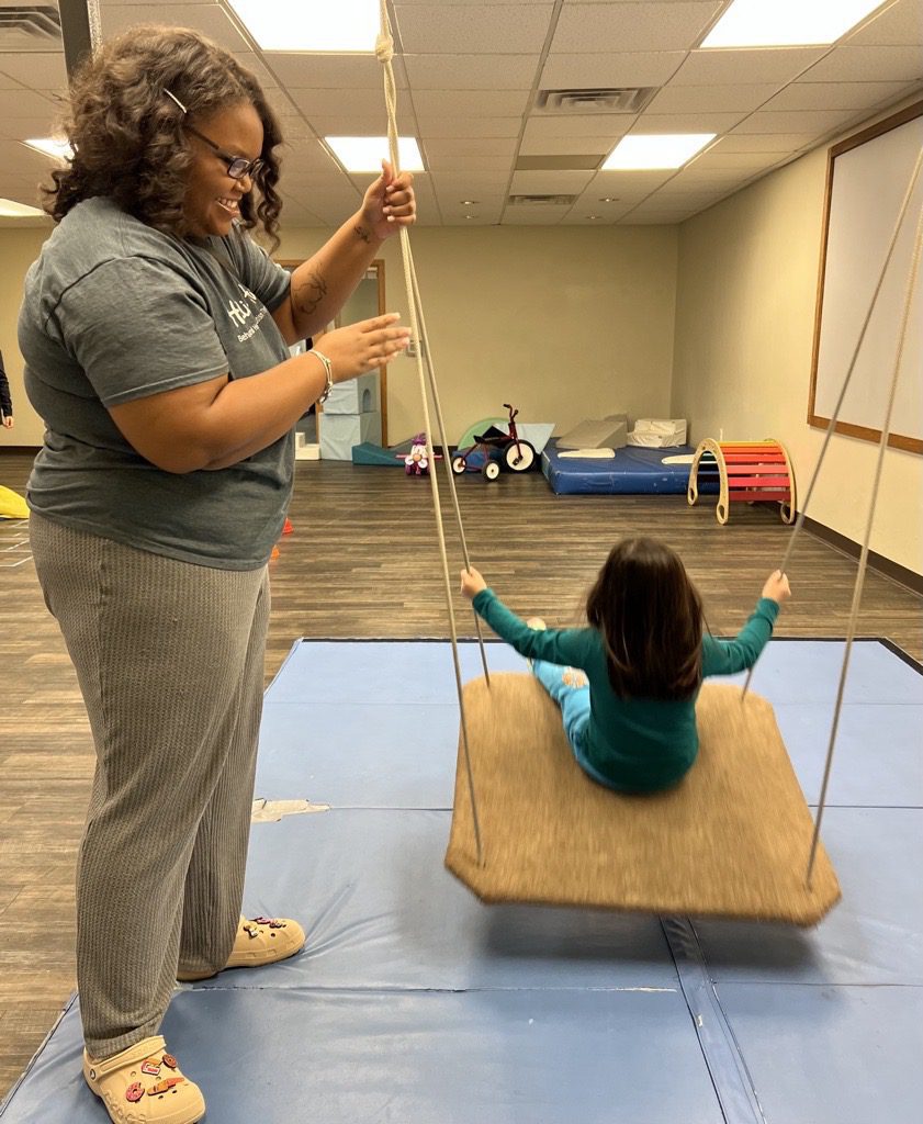 Registered Behavior Technician pushing child/client in swing. 