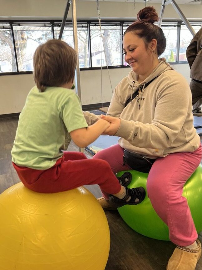 Registered Behavior Technician bouncing on ball with child/client.